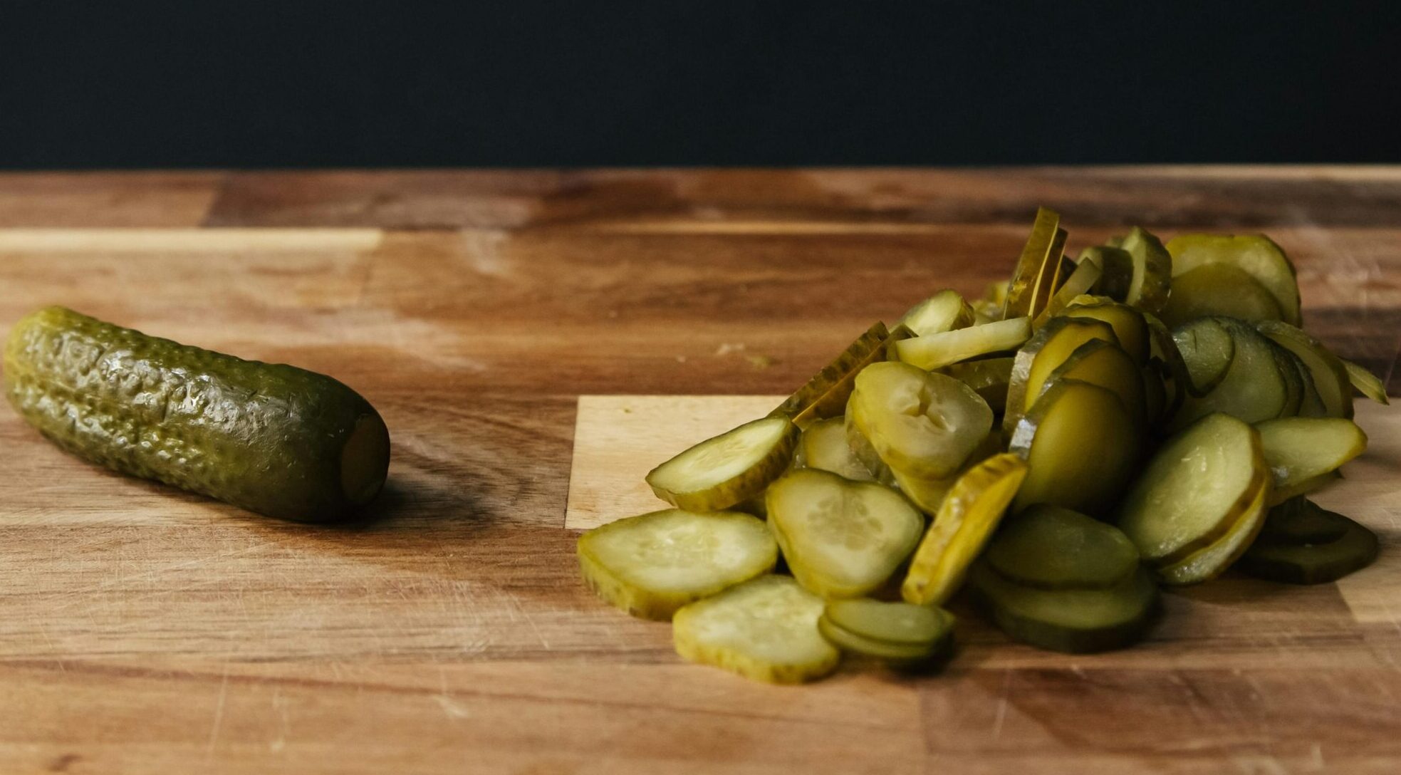 Sliced pickles on a wooden board with rustic background, highlighting freshness and simplicity.