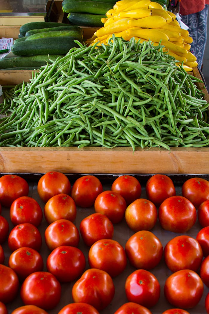 Fresh vegetables including green beans, tomatoes, zucchini, and squash neatly arranged at a market.